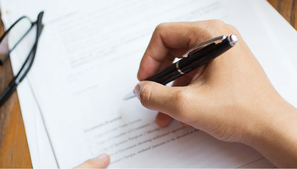 a hand with a pen filling out documents